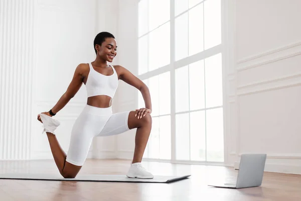Fröhlich schwarze Frau dehnt Beinmuskeln mit PC — Stockfoto