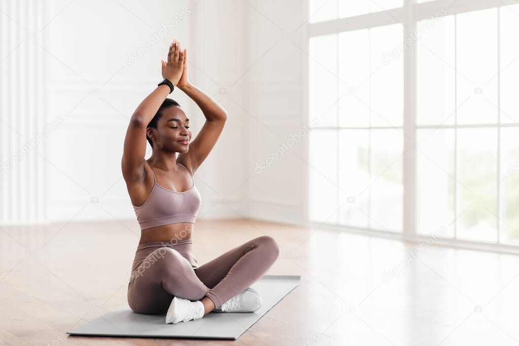 Young black woman sitting in lotus position on mat