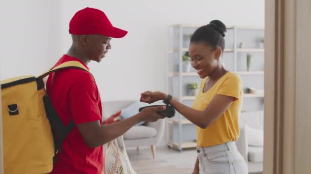 Service de livraison d'épicerie. Courrier afro-américain positif en uniforme rouge donnant paquet avec des aliments frais à dame noire — Video