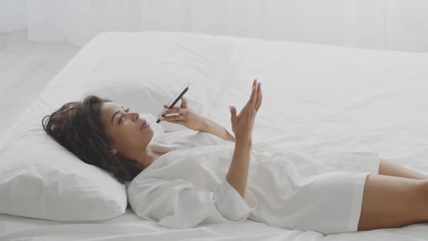 Communication moderne dans les messagers. Jeune femme afro-américaine enregistrant un message audio sur smartphone, couchée au lit — Video