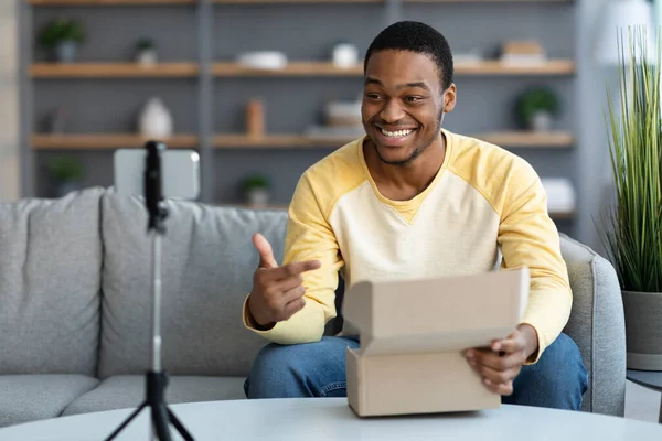 Chico negro guapo transmitiendo desde casa, usando teléfono inteligente en el trípode —  Fotos de Stock