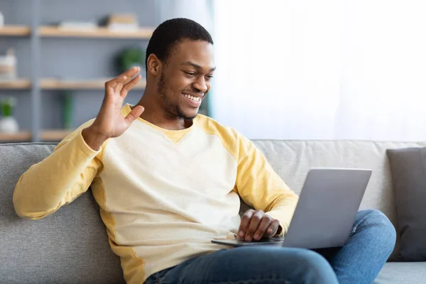 Alegre chico negro saludando en la pantalla del ordenador portátil, interior del hogar — Foto de Stock