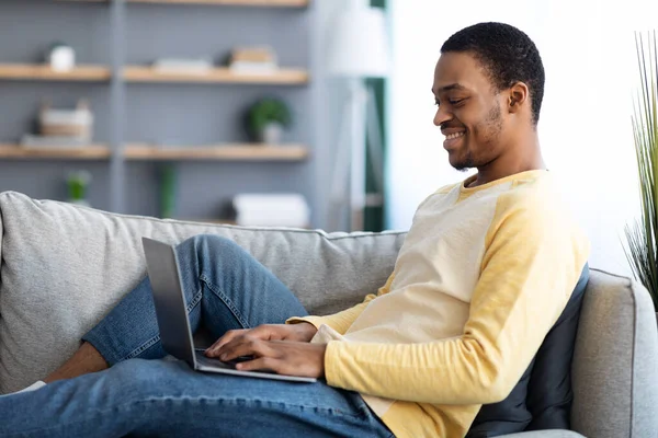 Feliz hombre negro disfrutando de su trabajo remoto, utilizando el ordenador portátil — Foto de Stock