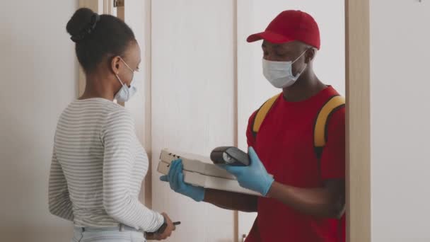 Služba rychlého občerstvení. Africký americký kurýr v uniformě nosí ochrannou masku a rukavice dává pizzu ženě — Stock video