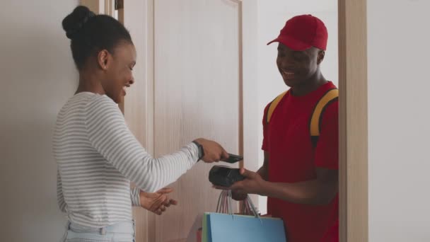 İnternetten alışveriş ve teslimat. Afrikalı Amerikalı bir kadın, elbiselerini kredi kartıyla ödüyor, ev alışverişlerinin keyfini çıkarıyor. — Stok video