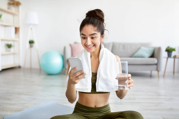 Ritratto di giovane donna indiana con vetro d'acqua e web di navigazione smartphone, controllare i social media a casa — Foto Stock