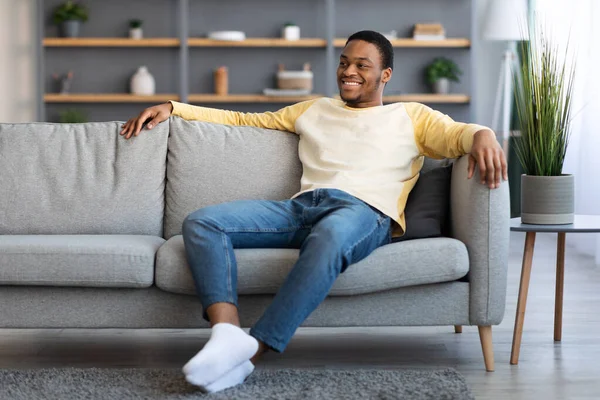 Radostný africký Američan sedí na pohovce doma — Stock fotografie