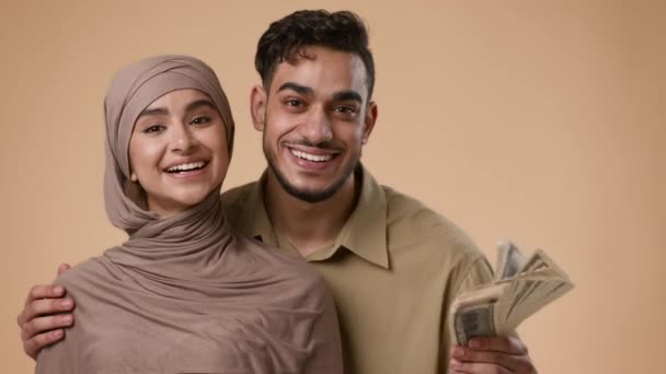Feliz pareja musulmana rica sosteniendo dinero en efectivo sobre fondo beige — Vídeo de stock