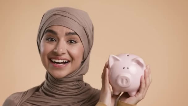 Glad Muselman Lady Skaka Piggybank Full av pengar, Beige bakgrund — Stockvideo