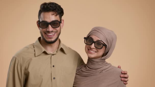 Alegre pareja musulmana con gafas de sol posando abrazando sobre fondo beige — Vídeo de stock