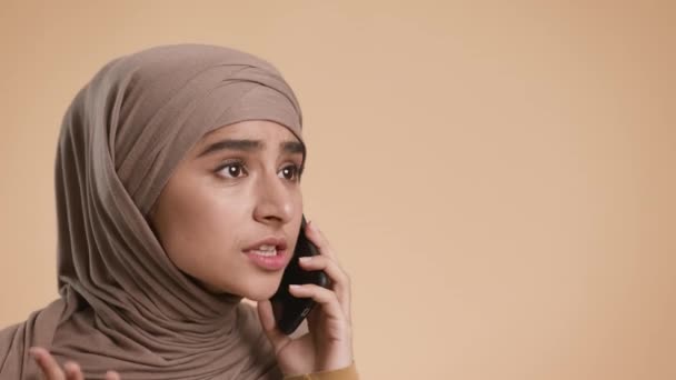 Emocional mujer musulmana descontenta hablando por teléfono sobre fondo beige — Vídeo de stock