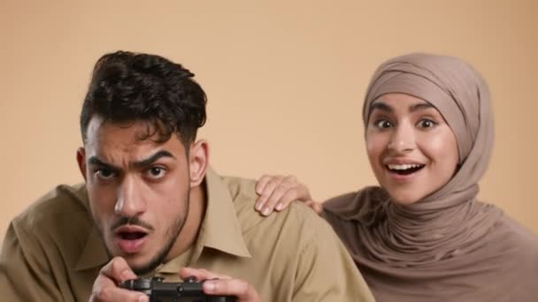 Мусульманская пара тысячелетия, играющая в видеоигры на фоне бежевой студии — стоковое видео