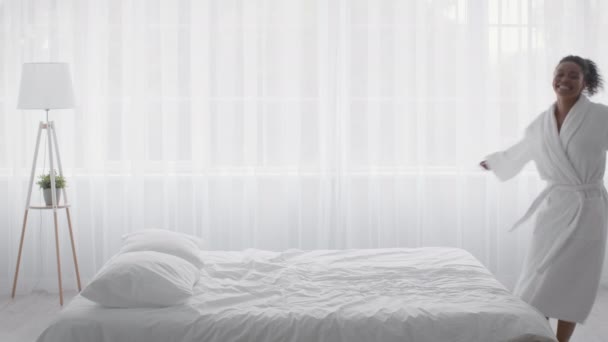 Äntligen semester. Ung glad afrikansk amerikansk kvinna faller ner på vit säng, njuter av nya mysiga linne i hotellrummet — Stockvideo