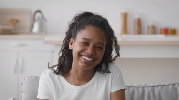 Tiszta boldogság. Boldog pozitív tini afro-amerikai lány nevet a kamera, ül otthon, közelről portré — Stock videók