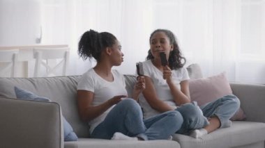 Yaz aldatmacası yemeği. İki Afrikalı Amerikalı genç kız kardeş dondurma yiyor, kanepede oturup sohbet ediyorlar.