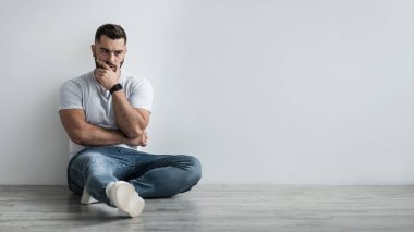 Depresyondaki genç adam evde gri duvara yaslanmış, mutsuz, yalnız ve depresyonda.