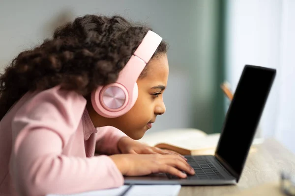 Conceito de juventude e tecnologia. Estudante preto focado usando computador portátil, sentado à mesa muito perto do PC, vista lateral — Fotografia de Stock