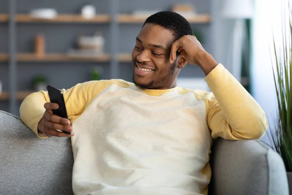 Hombre americano africano alegre que se enfría en casa, usando el teléfono inteligente — Foto de Stock