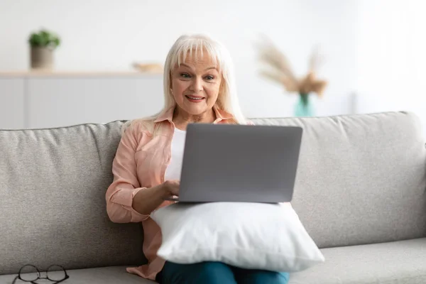 Szczęśliwy Dojrzałe kobieta siedzi na kanapie i za pomocą komputera — Zdjęcie stockowe