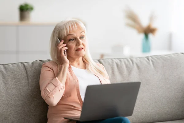 Зрелая женщина работает и разговаривает по мобильному телефону дома — стоковое фото