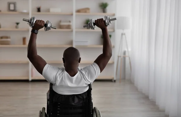 Afrikai-amerikai fogyatékos férfi ül tolószékben, és gyakorló berendezések otthon, fitt és edzés — Stock Fotó