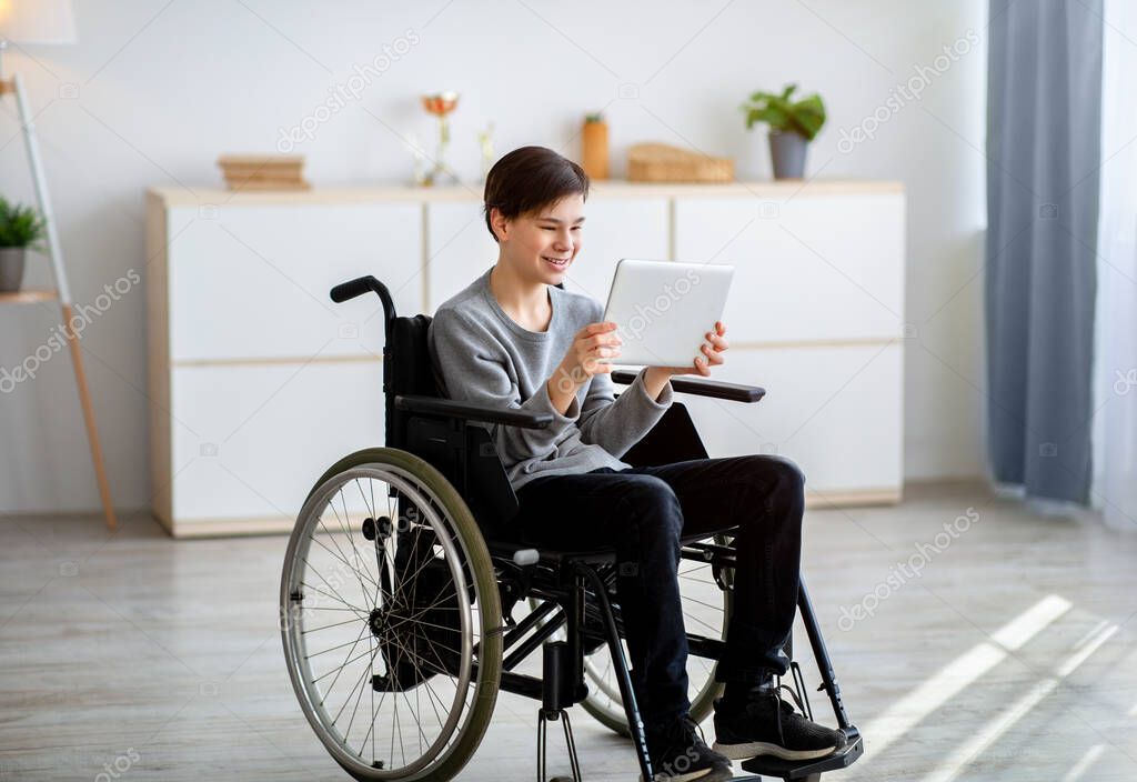 Web-based education. Joyful teenage student in wheelchair with tablet pc having online lesson at home