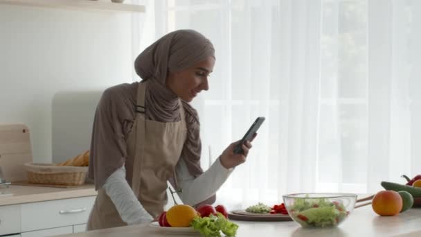 キッチンで料理をしながら写真を撮るムスリム女性 — ストック動画