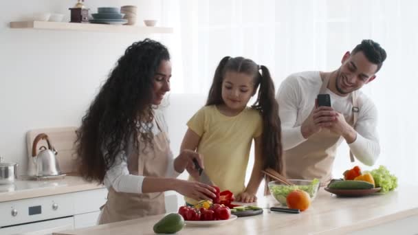 Arabiska mannen tar foto medan fru och dotter matlagning inomhus — Stockvideo