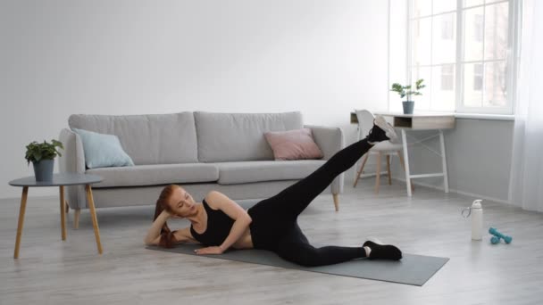 Sportliche Weibchen tun Side Leg Raise auf dem Boden zu Hause — Stockvideo