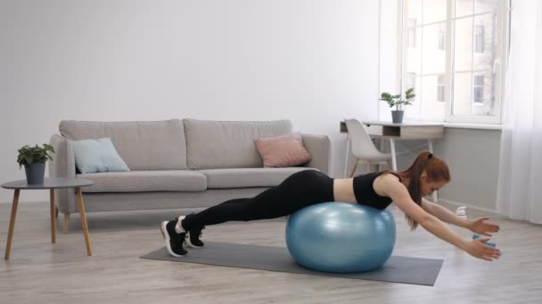 Lady haciendo ejercicio sobre la pelota levantando brazos acostada en el estómago en interiores — Vídeos de Stock