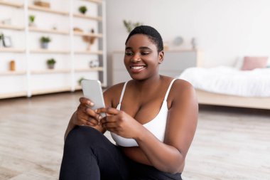 Gezici cihaz kullanan kıvrımlı siyahi kadın, ev içi eğitimden sonra, kapalı alanda