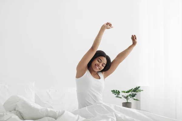 Mulher negra feliz cheio de vitalidade e energia, acordar e esticar as mãos, sentado na cama e sorrindo, espaço cópia — Fotografia de Stock