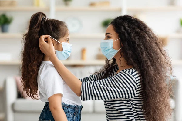 Vista lateral de la mujer poniendo mascarilla en su hija —  Fotos de Stock