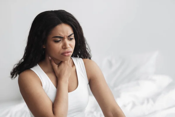 Concepto de salud. Triste mujer afroamericana enferma tosiendo, sufriendo de dolor de garganta, sentada en la cama en casa — Foto de Stock