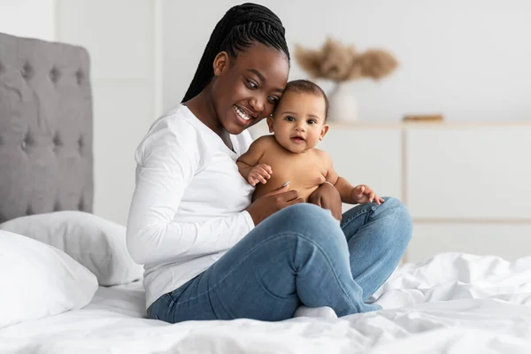 Negro mami sentado con su lindo pequeño bebé en la cama —  Fotos de Stock