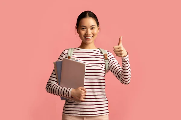 Portrait de joyeux asiatique femme étudiant tenant des classeurs et montrant pouce vers le haut — Photo