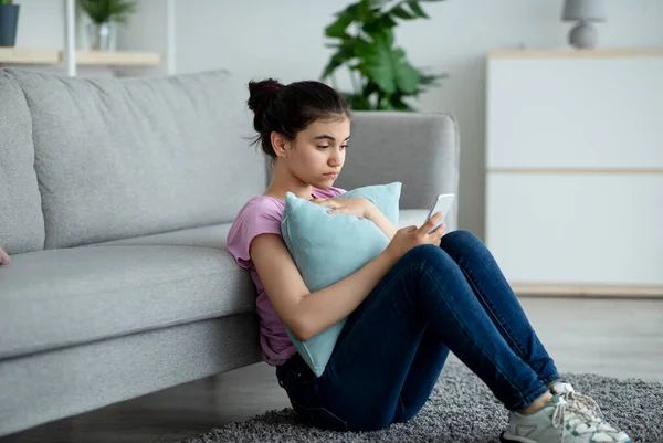 Gespannen indiaanse tiener meisje zitten op de vloer met mobiele telefoon en het lezen van slechte boodschap thuis — Stockfoto