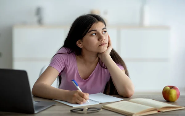 Chica adolescente india reflexiva que estudia en línea desde casa, tomando notas durante la lección web, sintiéndose aburrido en casa, panorama — Foto de Stock