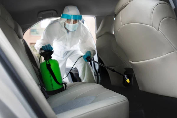 Trabajador en traje de materiales peligrosos con limpieza química de aerosol de alcohol dentro del coche para desinfectar — Foto de Stock