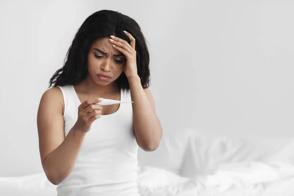 Feber, behandling hemma. Upprörd sjuk svart kvinna kontrollera kroppstemperatur hålla och titta på termometer, kopiera utrymme — Stockfoto