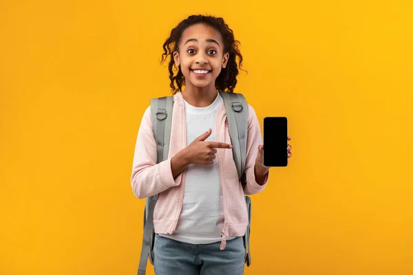 Захоплена чорна дівчина показує порожній екран смартфона і вказує — стокове фото