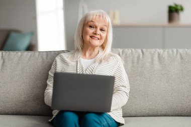 Kanepede oturan ve bilgisayar kullanan olgun bir kadın.