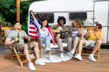 Gitar çalan, şarkı söyleyen, kamp yapan, karavan yakınlarında milli Amerikan bayramını kutlayan bir grup genç arkadaş.