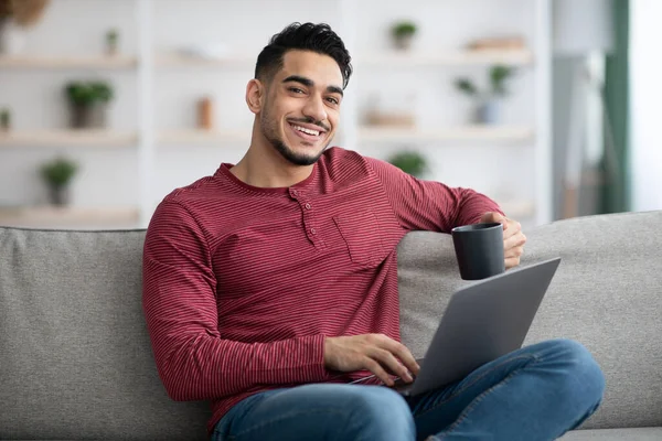 Entspannter Araber sitzt zu Hause auf Couch und benutzt Laptop — Stockfoto