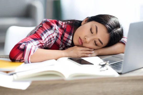 Измученная азиатская студентка спит за столом с книгами и ноутбуком — стоковое фото