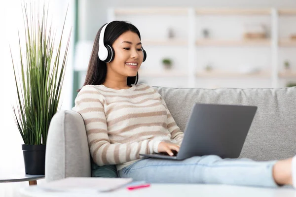Joven mujer asiática freelancer en auriculares trabajando a distancia con el ordenador portátil en casa — Foto de Stock