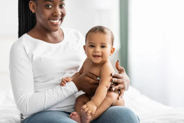 Svart mamma sitter med sitt söta lilla barn på sängen — Stockfoto