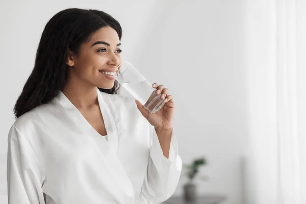 Nutrição útil e equilíbrio de água para a pele. Millennial Africano americano mulher em roupão de banho de água potável, espaço vazio — Fotografia de Stock