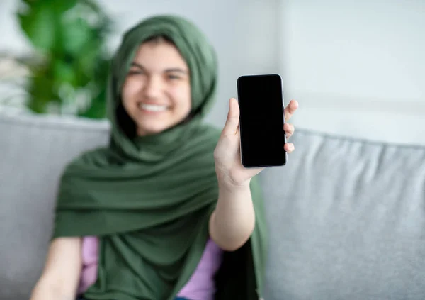 イスラム教徒のティーン女の子でヒジャーブ州の携帯電話を示す自宅で空白の画面、モックアップのためのモバイルアプリやウェブサイトのデザイン — ストック写真