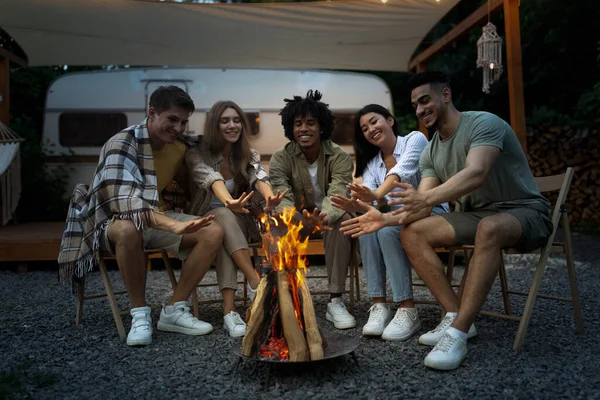 Millénaire divers amis assis près de feu de joie, mains chaudes, avoir du plaisir ensemble la nuit sur le voyage de camping — Photo